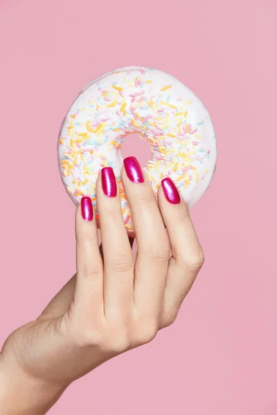 Maniküre. Hand mit rosa Nägeln hält Donut — Stockfoto