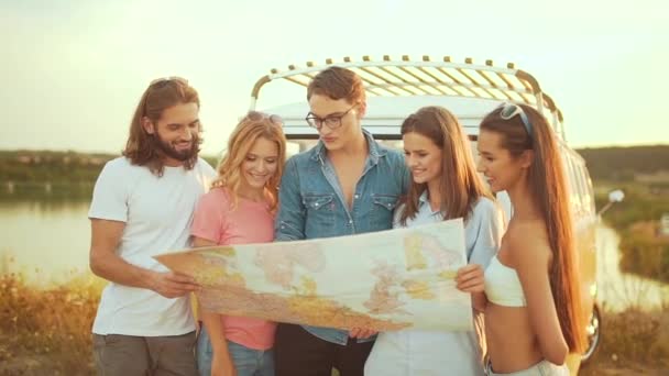 夏に車の近くの地図を持つ若者 検索先の地図 休暇で旅行するには自然を楽しんで幸せな笑みを浮かべて友人のグループ 男性と女性の週末旅行 — ストック動画