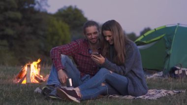 Turist çift cep telefonu, doğada kamp yakınındaki romantik kaçamaklar sahip bakarak aşık.