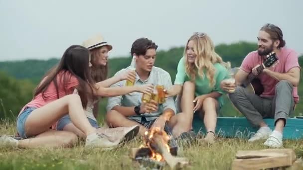 ビールを飲み 楽しい幸せな若いお友達とピクニック アウトドアで焚き火のそばに座って — ストック動画