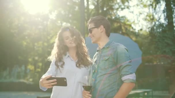 酒と写真を撮ると夏の週末に自然で楽しい携帯電話のガラスと幸せなカップル — ストック動画