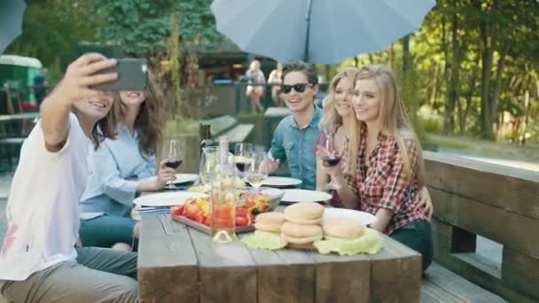 自然の中の夏の週末にテーブルに座って携帯電話で写真を撮るとワインを飲んで友人のグループ — ストック動画