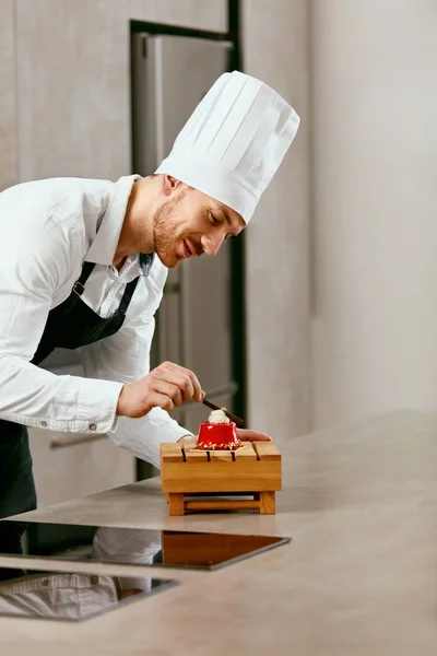 Male Pastry Cook Decorating Dessert In Kitchen