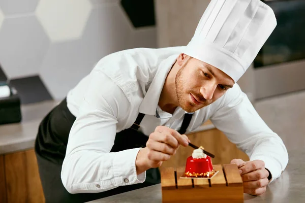 Male Pastry Cook Decorating Dessert In Kitchen