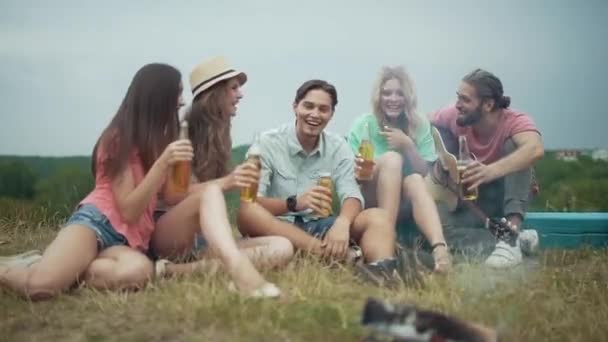 Happy vrienden drinken bier, plezier en zitten in de buurt vreugdevuur — Stockvideo