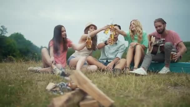 快乐的朋友喝啤酒, 有乐趣, 坐在篝火旁 — 图库视频影像