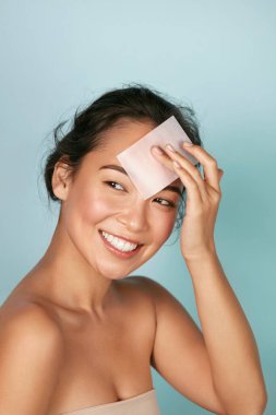Face skin care. Smiling woman using oil blotting paper portrait clipart