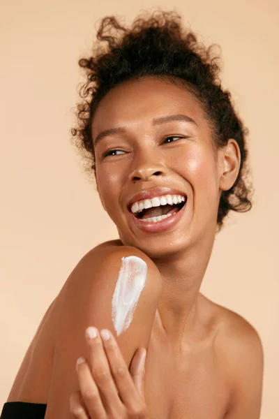 Body skin care. Smiling black woman applying body cream portrait