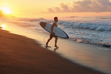 Sörfçü. Okyanus dalgalarında sörf yapan sörf tahtası olan sörfçü adam. Sandy Beach, Bali 'de güzel bir gün doğumu. Aktif Yaşam Tarzı İçin Su Sporu.