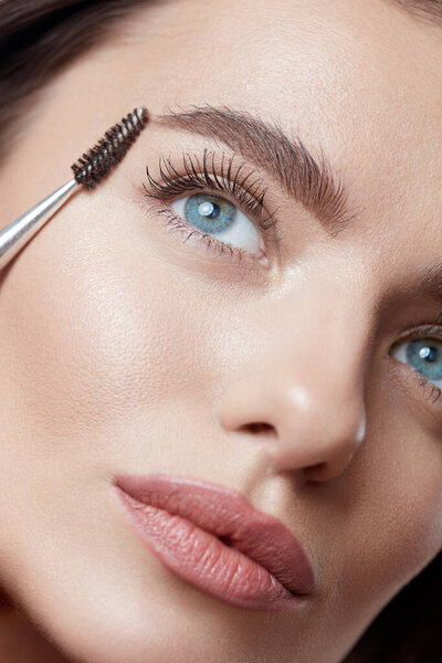 Beauty. Woman Brushing Eyebrows With Brush. Close Up Portrait Of Beautiful Girl. Blue-Eyed Brunette With Perfect Skin And Natural Makeup. 