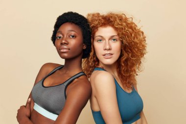 Fitness Women. Ethnic Sporty Girls Close Up Portrait. Beautiful Brunette And Redhead Posing On Beige Background. Sport For Active Lifestyle.  clipart