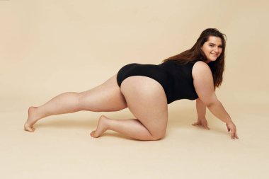 Artı Beden Modeli. Siyah elbiseli şişman kadın portresi. Bej arka planda sürünen esmer poz. Vücut Pozitif Kavram. 