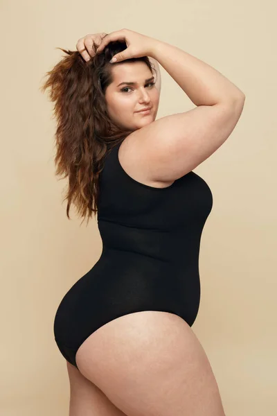 加尺寸模型 黑衣胖女人的肖像 布鲁内特触摸头发和看着相机 关于米色背景的身体正面概念 — 图库照片