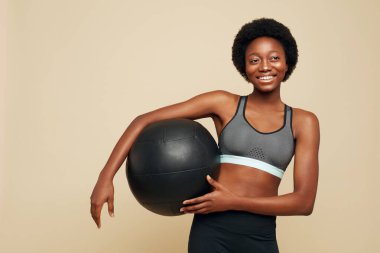 Fitness. Spor Afrikalı Kadın Portresi. Spor Giyim 'de gülümseyen, elinde siyah spor salonu balosu tutan ve uzaklara bakan bir kadın. Doğal Güzellik için Spor.