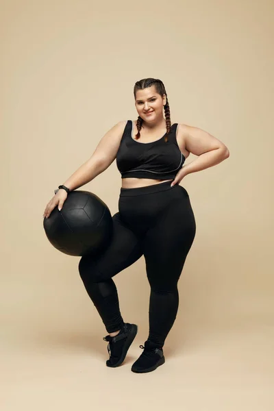 加尺寸模型 穿着黑色运动服的胖女人全长肖像 微笑布鲁内特举行健身球 身体积极与运动为生活方式 — 图库照片