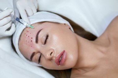 Yüz Güzelliği Tedavisi. Kadın alnına yaşlanma önleyici iğne vuruluyor. Tıp Kliniğinde Kozmetik Teni Teorisi.