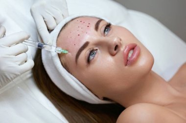Yüz bakımı. Alnına Yaşlanma Karşıtı Güzellik İğnesi. Kozmetik Kliniği 'nde cilt Gençleştirme Prosedürü. Şırıngayla Eldivenli Güzellik Uzmanı.