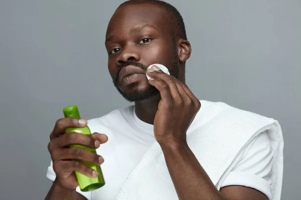 Face Care. Male African Model Cleans Facial Skin With Round Patch. Green Bottle With Cosmetic Tonic. Skincare Beauty Routine For Man.