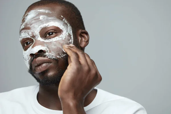 Face Treatment. Skin Care Procedure For Man. Model Applying White Facial Mask During Spa Relaxation. Cosmetology Mud For Facecare.