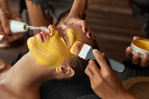 Face Mask. Beautician Applying Yellow Skin Care Product. Spa Beauty Treatment For Relaxed Woman.