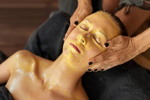 Leczenie Twarzy Odpoczywająca Kobieta Zabiegu Pielęgnacyjnym Beautician Stosując Żółtą Maskę — Zdjęcie stockowe