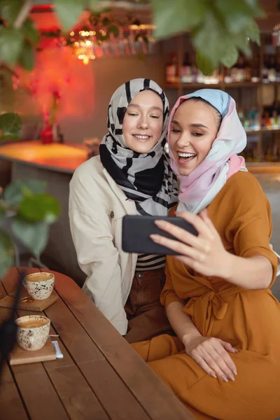 Friends. Women In Hijab Taking Selfie. Women Meeting In Cafe. Smiling Muslim Female Having Fun In Bistro.