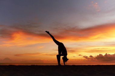 Yoga pozları. Asana 'yı ikiye bölen ya da Ocean Beach' te bir ayak yukarıda duran kadın. Bayan Siluet Urdhva Prasarita Eka Padasana 'yı Güzel Gün Batımında Alıştırıyor. Yaşam Tarzı Egzersizi olarak Yoga.