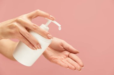 El hijyeni. Pembe arka plana karşı kadın eli içinde sıvı sabun şişesi. Virüsü önlemek için günlük kişisel hijyen rutini. Sağlıklı kalmak için ellerini yıka.. 