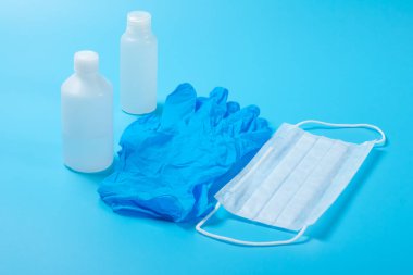 Tek kullanımlık tıbbi maske, antiseptik ve lateks eldiven açık mavi yüzeyde.