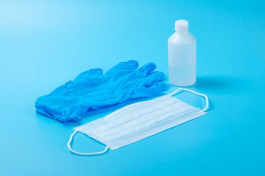 Tek kullanımlık tıbbi maske, antiseptik ve lateks eldiven açık mavi yüzeyde.