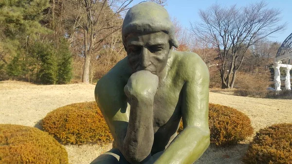 Green statue of thinker Auguste Rodin, setting naked on a rock