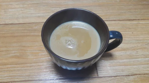 Vista superior de la leche té negro en una taza colocada sobre un piso de madera . —  Fotos de Stock