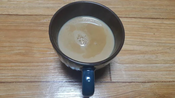 Vista superior de la leche té negro en una taza colocada sobre un piso de madera . —  Fotos de Stock