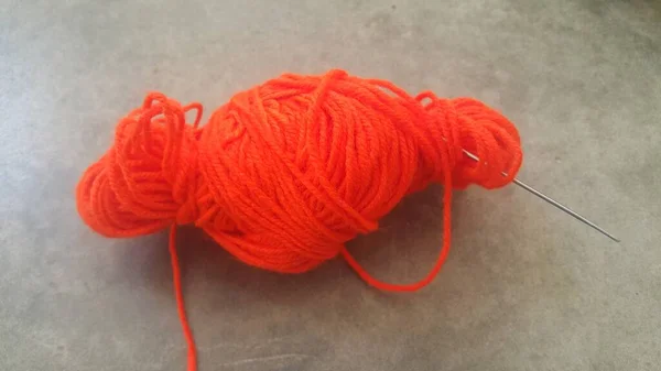 Orange ball of threads wool yarn for knitting on grey floor background