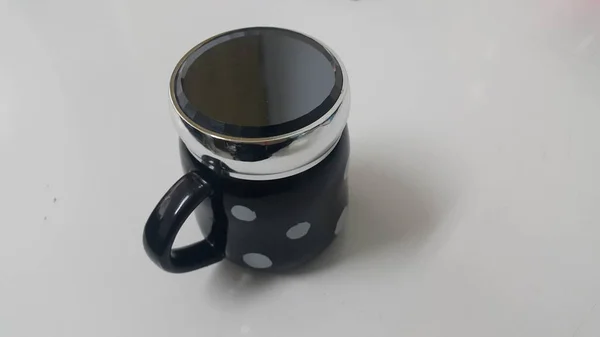 Belle tasse de café noir avec des points blancs sur le sol blanc avec couvercle noir dessus — Photo