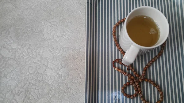 Vista superior del té verde en una taza con cuentas de oración o rosario colocado en una bandeja — Foto de Stock