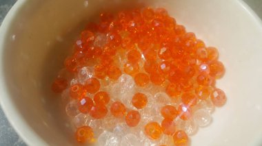 Bir kase içinde parlayan, şeffaf, turuncu renkli kristal boncuklar veya değerli taşlar