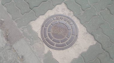 Asfalt yol altında drenaj veya kanalizasyon üzerinde bir rögar kapağı üst görünümü.