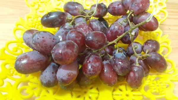 Close up view of bunches of brown grapes served in yellow plastic fruit tray — Stock Photo, Image