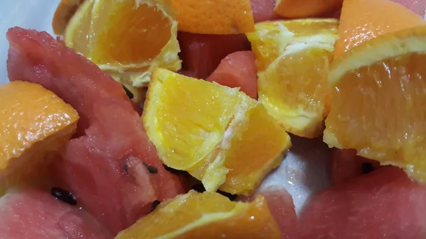 セラミックホワイトプレートに添えたオレンジと赤いスイカのミックスフルーツスライスのクローズアップビュー スイカは甘く オレンジは柑橘系の味わい — ストック写真