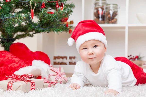 Schattige baby in een kerstmuts naast kerstboom met presenteert — Stockfoto