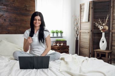 Yatağa rahatlatıcı. Bir fincan kahve zevk ve onu laptop kullanarak güzel kadın