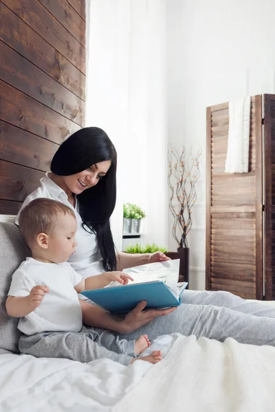 Child education. Happy mother with her toddler sitting on the bed and reading a book — Stock Photo, Image