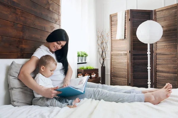 Barn utbildning. Lycklig mamma med hennes barn sitter på sängen och läsa en bok — Stockfoto