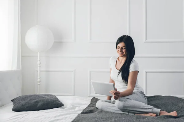 Красивая женщина отдыхает на кровати и с помощью планшета — стоковое фото