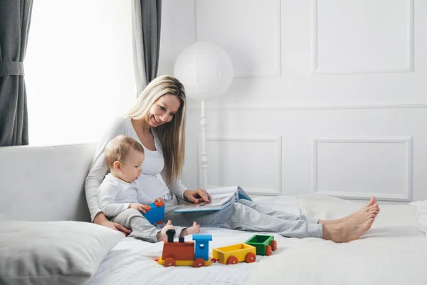Educaţie pentru copii. Mama fericita cu copilul ei stand pe pat si citind o carte — Fotografie, imagine de stoc