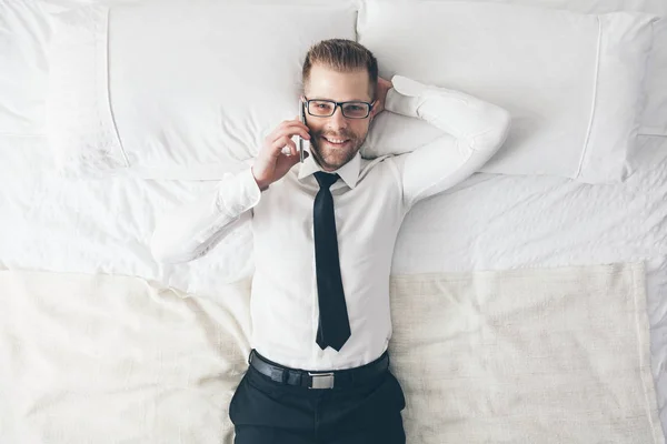 Ansicht von oben. schöner Geschäftsmann mit Brille auf dem Bett, der vom Telefon aus anruft — Stockfoto