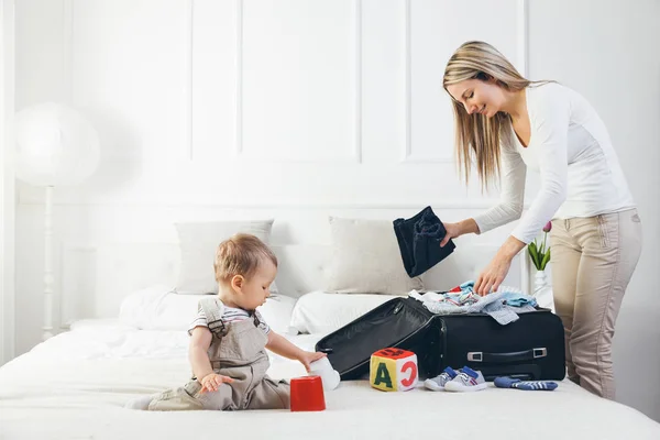 Voyager avec des enfants. Mère heureuse avec son enfant emballant des vêtements pour les vacances Images De Stock Libres De Droits