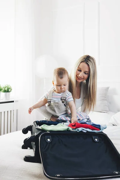 Reisen mit Kindern. glückliche Mutter mit ihrem Kind, das Kleidung für den Urlaub einpackt — Stockfoto