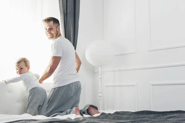 Lycklig far med sin son som spelar hemma på sängen — Stockfoto